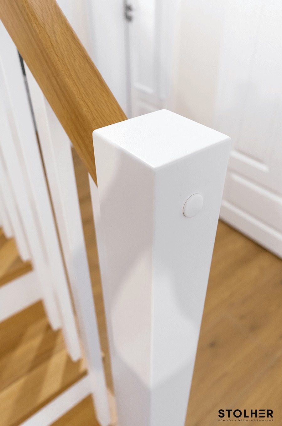 Biała balustrada schodów z drewnianym pochwytem, widok z góry na stopnie z jasnego drewna.