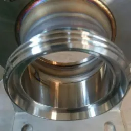 Spoina obwodowa na elemencie stalowym, widoczne przebarwienia termiczne po procesie łączenia metali, podstawa mocująca z otworem.