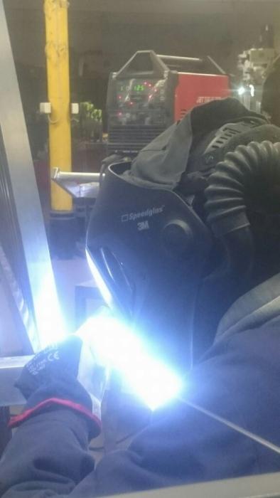 Praca w warsztacie: spawanie metalowej konstrukcji w masce ochronnej 3M Speedglas, widoczny spaw i urządzenie spawalnicze Jet Tig.