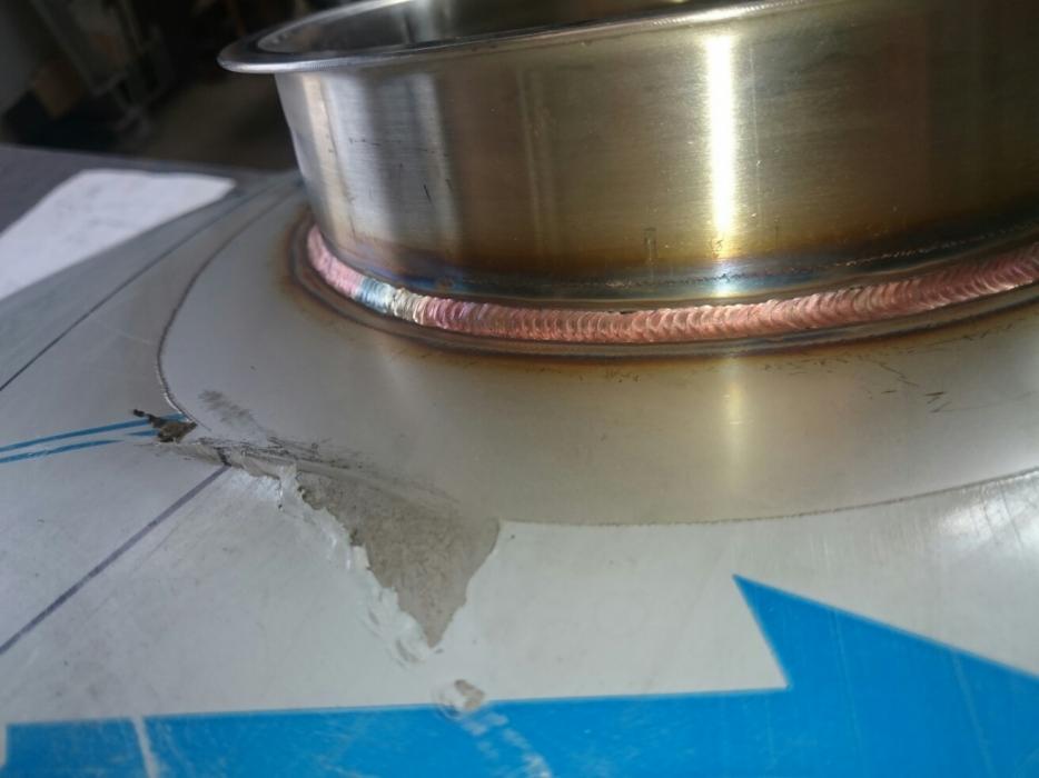 Szczegółowe zbliżenie spoiny łączącej metalowy kołnierz z powierzchnią, widoczne ślady obróbki i uszkodzenia powierzchni.