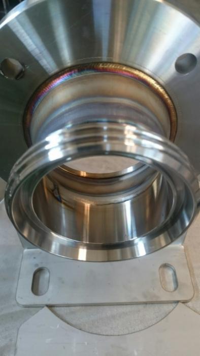 Spoina obwodowa na elemencie stalowym, widoczne przebarwienia termiczne po procesie łączenia metali, podstawa mocująca z otworem.