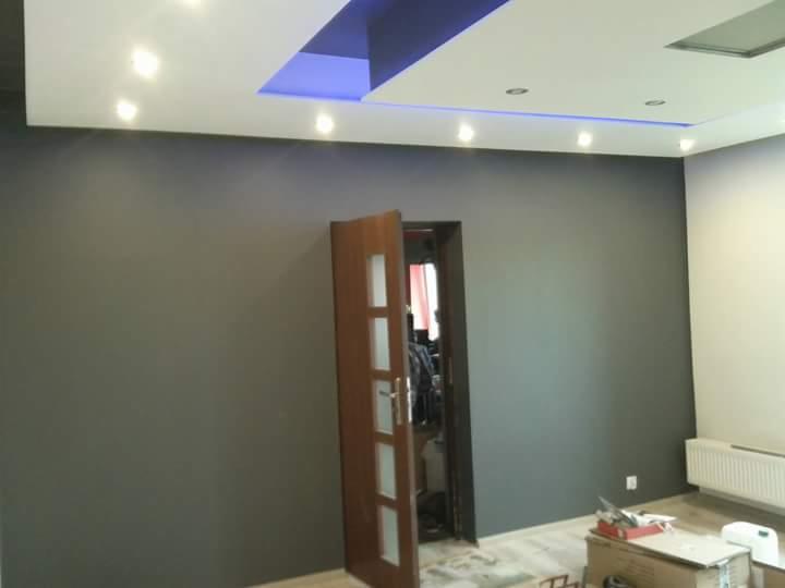 Wnętrze po malowaniu ścian na kolor szary, widoczny fragment podwieszanego sufitu z oświetleniem LED i otwarte drewniane drzwi z przeszkleniami.