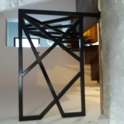 Czarna, metalowa konstrukcja o geometrycznym wzorze, prawdopodobnie fragment bramy lub ogrodzenia, w surowym wnętrzu w trakcie remontu w Nowej Soli.