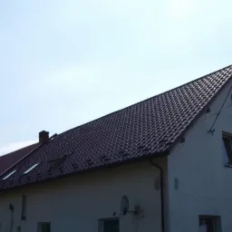 Dom z nowym, ciemnobrązowym dachem z dachówki, widoczne okna dachowe i komin.