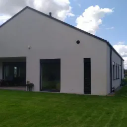 Nowoczesny, parterowy dom z płaskim dachem i dużymi oknami, widok z ogrodu w słoneczny dzień.