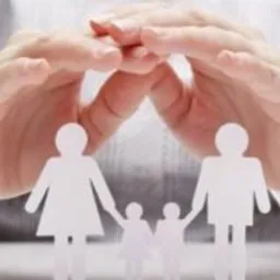 Dłonie tworzące ochronny gest nad papierowymi sylwetkami rodziny na jasnym tle.