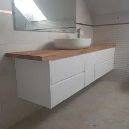 Nowoczesna łazienka w skandynawskim stylu: biała szafka pod umywalkę z drewnianym blatem, okrągła umywalka nablatowa, lustro odbijające skos dachu, płytki w odcieniach szarości.