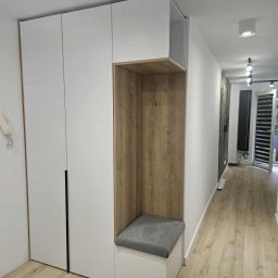 Meble na Wymiar DOMEB Łukasz Pamuła - Biała szafa wnękowa z siedziskiem i drewnianą wnęką w przedpokoju. Minimalistyczny design, jasne drewno na podłodze, nowoczesne oświetlenie sufitowe.