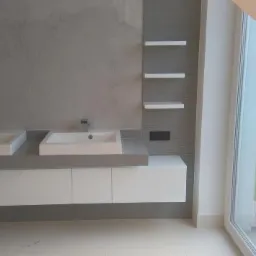 Nowoczesna łazienka z dwoma prostokątnymi umywalkami nablatowymi, szarą ścianą z delikatnym wzorem, białymi szafkami pod umywalkami i otwartym oknem balkonowym z widokiem na zieleń.