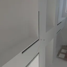 Wnętrze po remoncie, świeżo pomalowane na biało, z widocznymi detalami architektonicznymi i oknem zabezpieczonym folią.