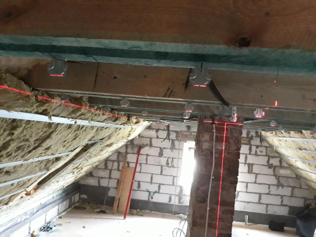 Montaż metalowego stelaża pod płyty na poddaszu z widoczną izolacją, poziomowany laserowo.