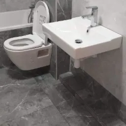 Nowoczesna łazienka z szarymi marmurkowymi płytkami, wisząca toaleta i umywalka z chromowaną baterią; narzędzia widoczne na zabudowie toalety.