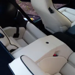 Jasna, skórzana tapicerka tylnych siedzeń Porsche 928 z czarnymi akcentami, widoczny pas bezpieczeństwa i zagłówek. Częściowo widoczna butelka z preparatem do czyszczenia tapicerki.