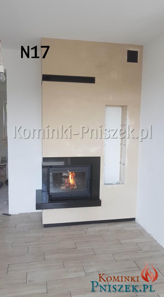 Nowoczesny wkład kominkowy z czarną obudową i płomieniami wewnątrz, wkomponowany w beżową ścianę z dekoracyjnymi elementami, na podłodze jasne płytki imitujące drewno.