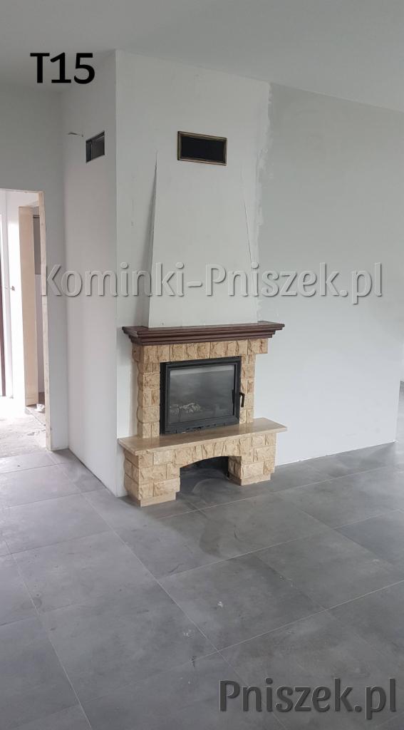 Kamienny wkład kominkowy z drewnianym obramowaniem, widoczny na tle surowych, szarych ścian i podłogi w nowym budynku, z widocznymi śladami prac wykończeniowych.