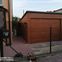 STALMAR MS - Nowy, drewnopodobny, brązowy budynek gospodarczy z płaskim dachem, widoczny przez siatkę ogrodzeniową na tle domu z otwartymi drzwiami wejściowymi i skrzynką pocztową o numerze 16.