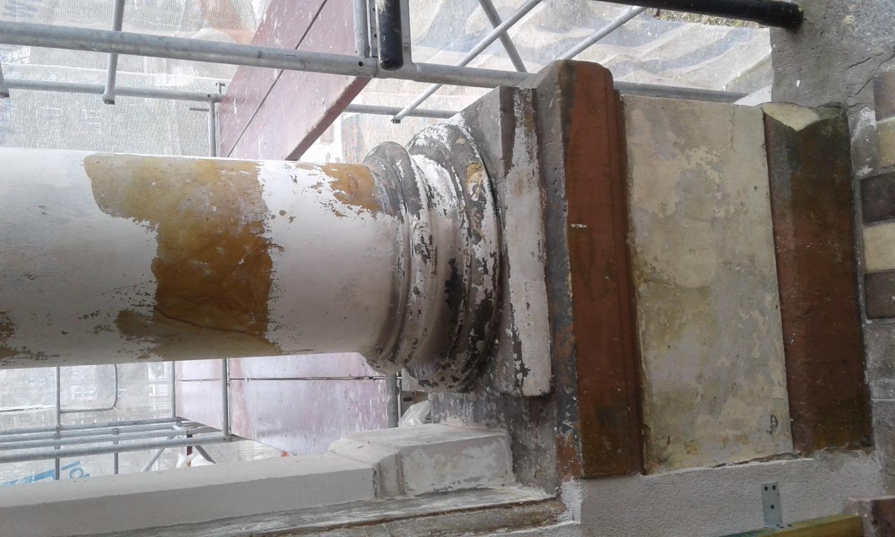 Fragment kolumny z dekoracyjnym kapitelem w trakcie renowacji, widoczne ślady starej farby i fragment rusztowania.