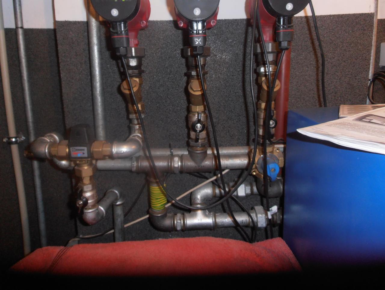 Węzeł cieplny z trzema pompami obiegowymi, zaworami i rurami, widok na instalację w kotłowni.