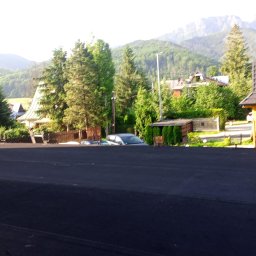 Krystian Biały - Hydroizolacje Usługi dekarskie -HYDRODACHY - Ciemna, nowa papa na dachu w kontraście z zielonym krajobrazem górskim w tle, widoczne domy i drzewa.