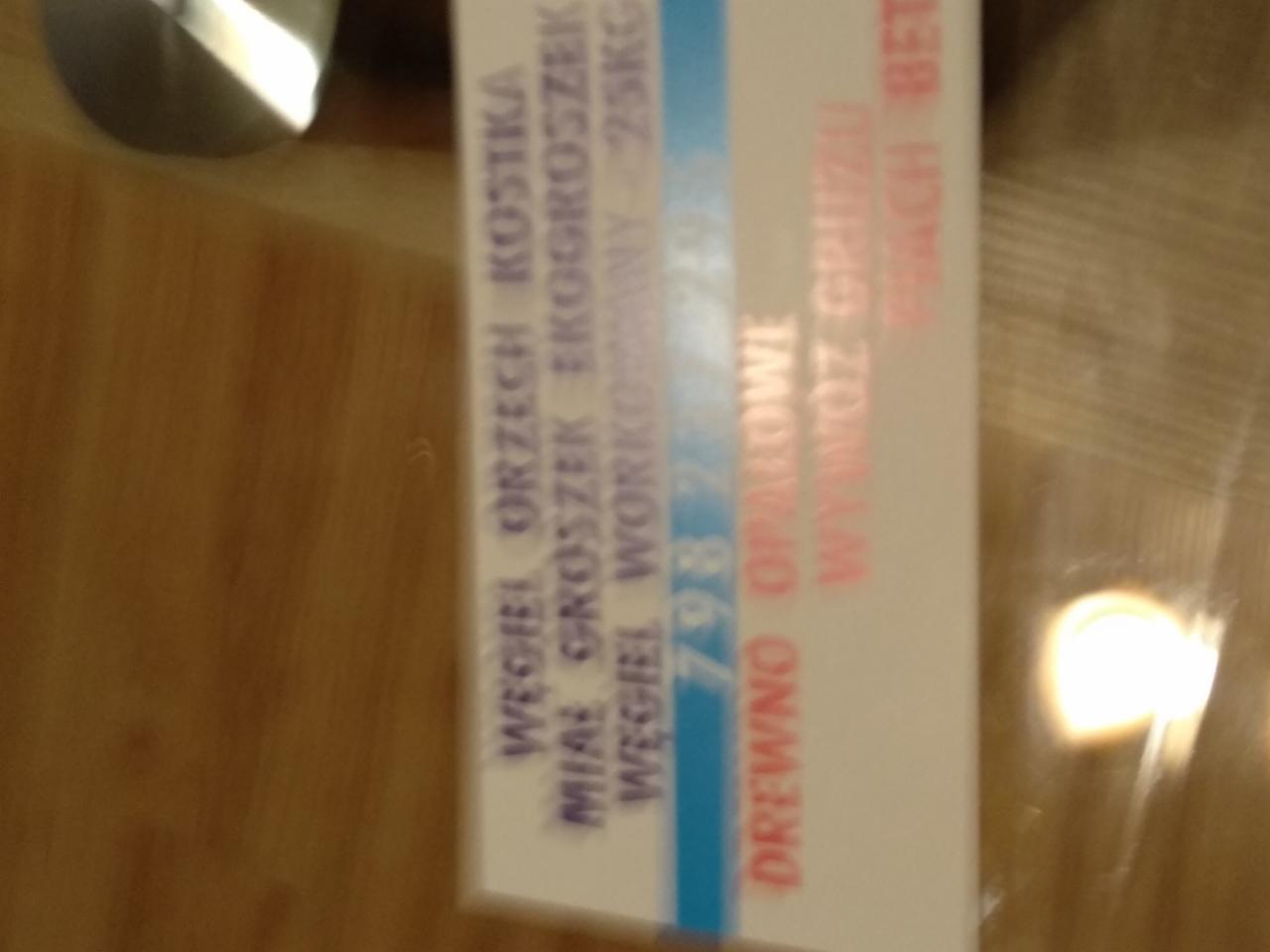 Etykieta na worku z informacją o zawartości: węgiel, drewno opałowe i wywóz gruzu, widoczna na drewnianym stole.