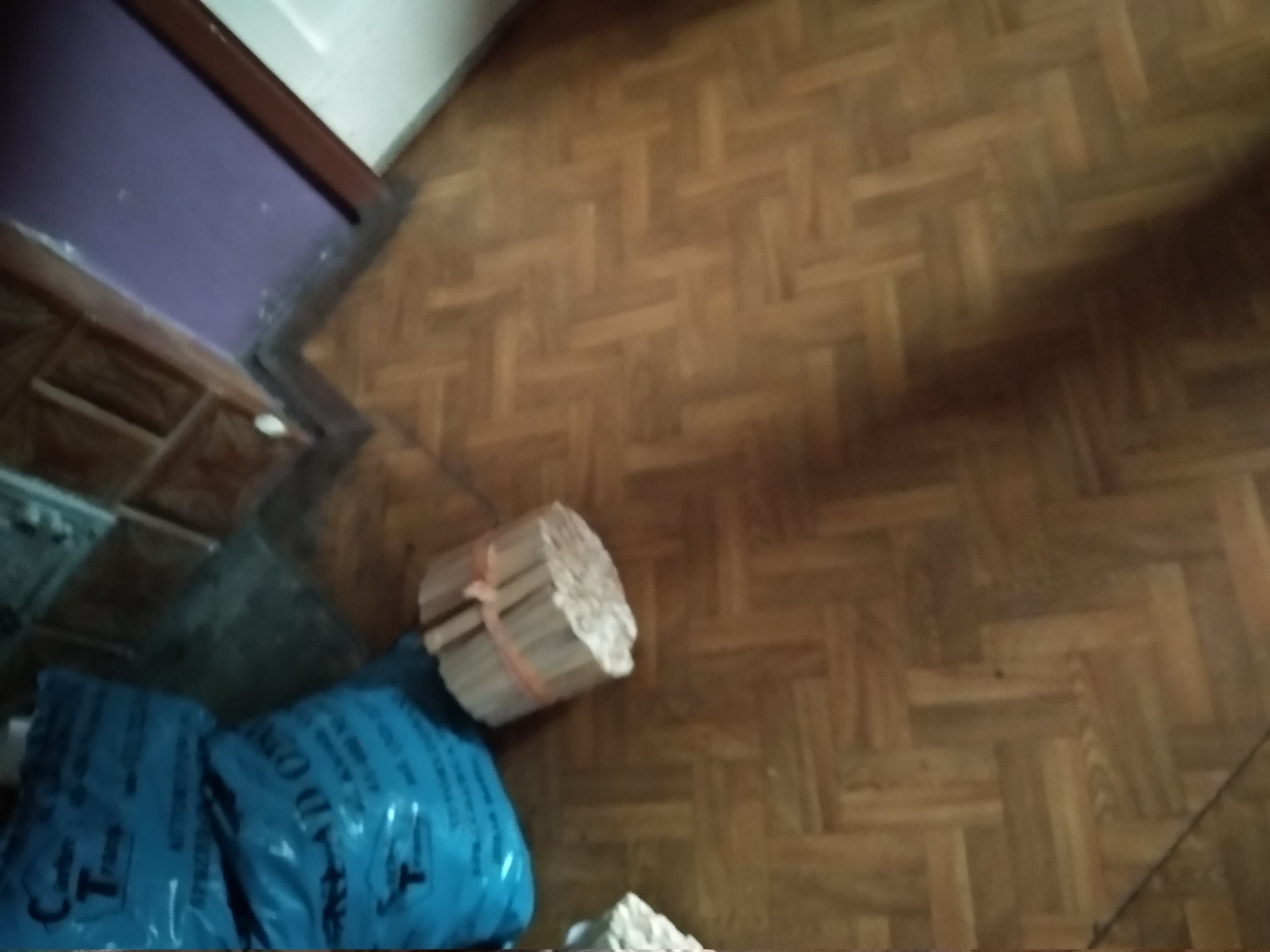 Niebieskie worki z gruzem i paczka związanych listew przypodłogowych leżą na parkiecie w rogu pomieszczenia.