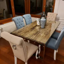 Stół jadalny z blatem z drewna i szkła, otoczony sześcioma krzesłami tapicerowanymi w odcieniach beżu i błękitu, z dekoracyjnymi przeszyciami i metalowymi detalami, na tle drewnianej podłogi.