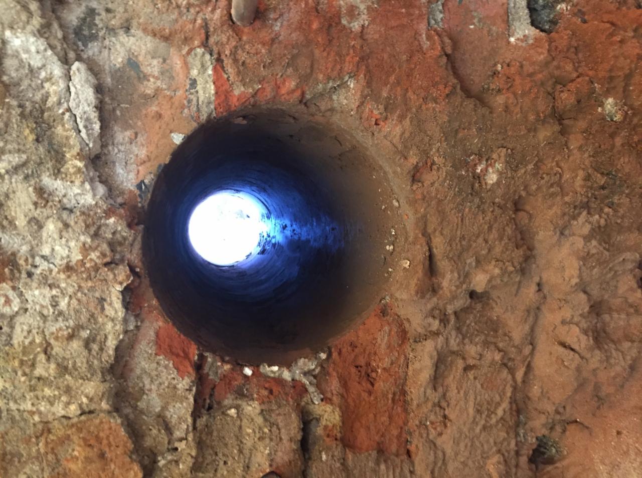 Otwór wywiercony w starej, ceglanej ścianie, z widocznym światłem na końcu tunelu.