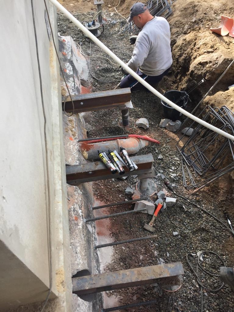 Wzmocnienie ściany wykopu za pomocą stalowych belek i kotew, widoczny robotnik przy pracy oraz narzędzia i materiały budowlane.