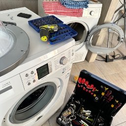 REPER24 SPÓŁKA Z OGRANICZONĄ ODPOWIEDZIALNOŚCIĄ - Rozłożona pralka z otwartymi drzwiczkami, obok skrzynka narzędziowa i wkrętarka. Widoczne ślady użytkowania na obudowie. W tle suszarka z tekstyliami.