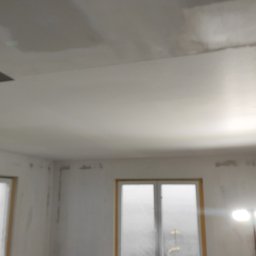 LUX&ART WNĘTRZA ŁUKASZ WĘGLOWSKI - Wnętrze w trakcie remontu: wyszpachlowany sufit, ściany przygotowane do malowania, okno z folią ochronną, podłoga zabezpieczona. Widoczne etapy prac wykończeniowych.