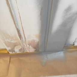 LUX&ART WNĘTRZA ŁUKASZ WĘGLOWSKI - Fragment ściany z listwami przypodłogowymi w trakcie szpachlowania, zabezpieczonej taśmą i papierem malarskim. Widoczne niedoskonałości i miejsca po szpachli.