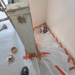 LUX&ART WNĘTRZA ŁUKASZ WĘGLOWSKI - Schody zabezpieczone folią malarską przed pracami. Widoczna puszka z farbą, wałek i pędzel. Fragment buta pracownika w dolnym rogu kadru. Jasne ściany.