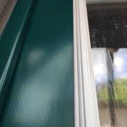 LUX&ART WNĘTRZA ŁUKASZ WĘGLOWSKI - Pomazana zielona framuga okienna z białym obramowaniem, widoczna z bliska, z refleksami światła na świeżej farbie.