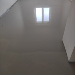 LUX&ART WNĘTRZA ŁUKASZ WĘGLOWSKI - Wylana, gładka posadzka samopoziomująca w pokoju. Widoczne ściany i okno odbijające się w mokrej powierzchni. Na podłodze brak jakichkolwiek zanieczyszczeń.