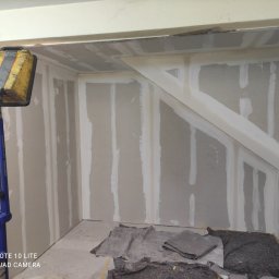 LUX&ART WNĘTRZA ŁUKASZ WĘGLOWSKI - Wnętrze w trakcie szpachlowania: płyty gipsowo-kartonowe z widocznymi łączeniami, oświetlone lampą budowlaną, przygotowane do dalszych prac wykończeniowych.