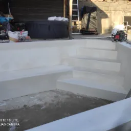 Białe schody basenowe po renowacji, widoczne narzędzia i akcesoria, drabina. W tle jacuzzi i elementy wyposażenia ogrodu. Jasne, naturalne światło.