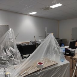 LUX&ART WNĘTRZA ŁUKASZ WĘGLOWSKI - Przygotowanie biura do malowania: meble i sprzęt zabezpieczone folią ochronną, widoczne narzędzia malarskie. Oświetlenie sufitowe.