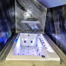 Nowoczesna wanna z hydromasażem, podświetlana LED, w łazience z dekoracyjną ścianą imitującą marmur. Wykończenie wnętrza w odcieniach szarości i bieli.