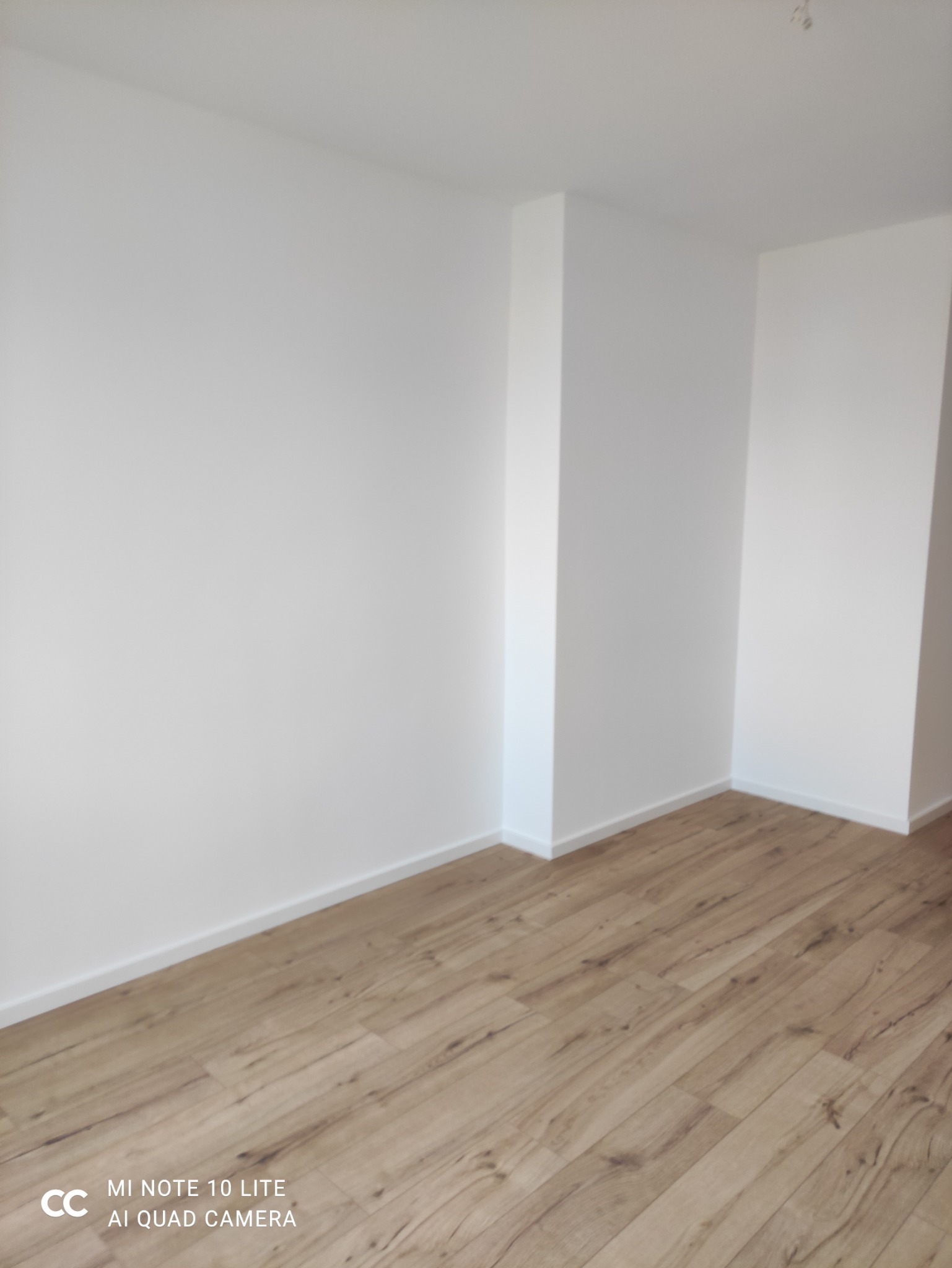 Jasne panele podłogowe ułożone w nowym, pomalowanym na biało pomieszczeniu. Widoczny fragment ściany z listwami przypodłogowymi.