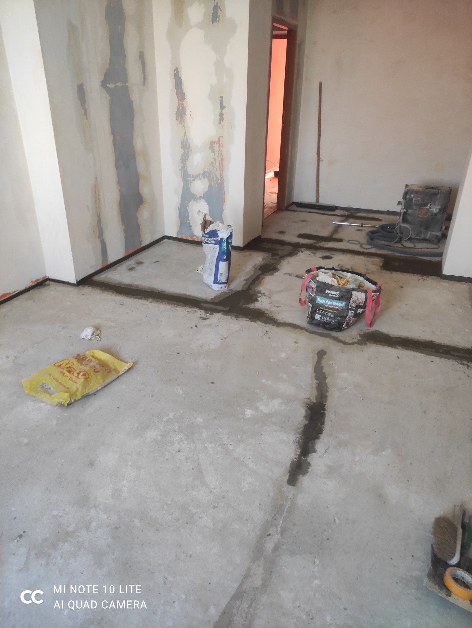 Przygotowanie podłoża: wylewka samopoziomująca w trakcie prac. Widoczne worki z zaprawą, narzędzia i ślady wylewki na podłodze. Ściany częściowo przygotowane.
