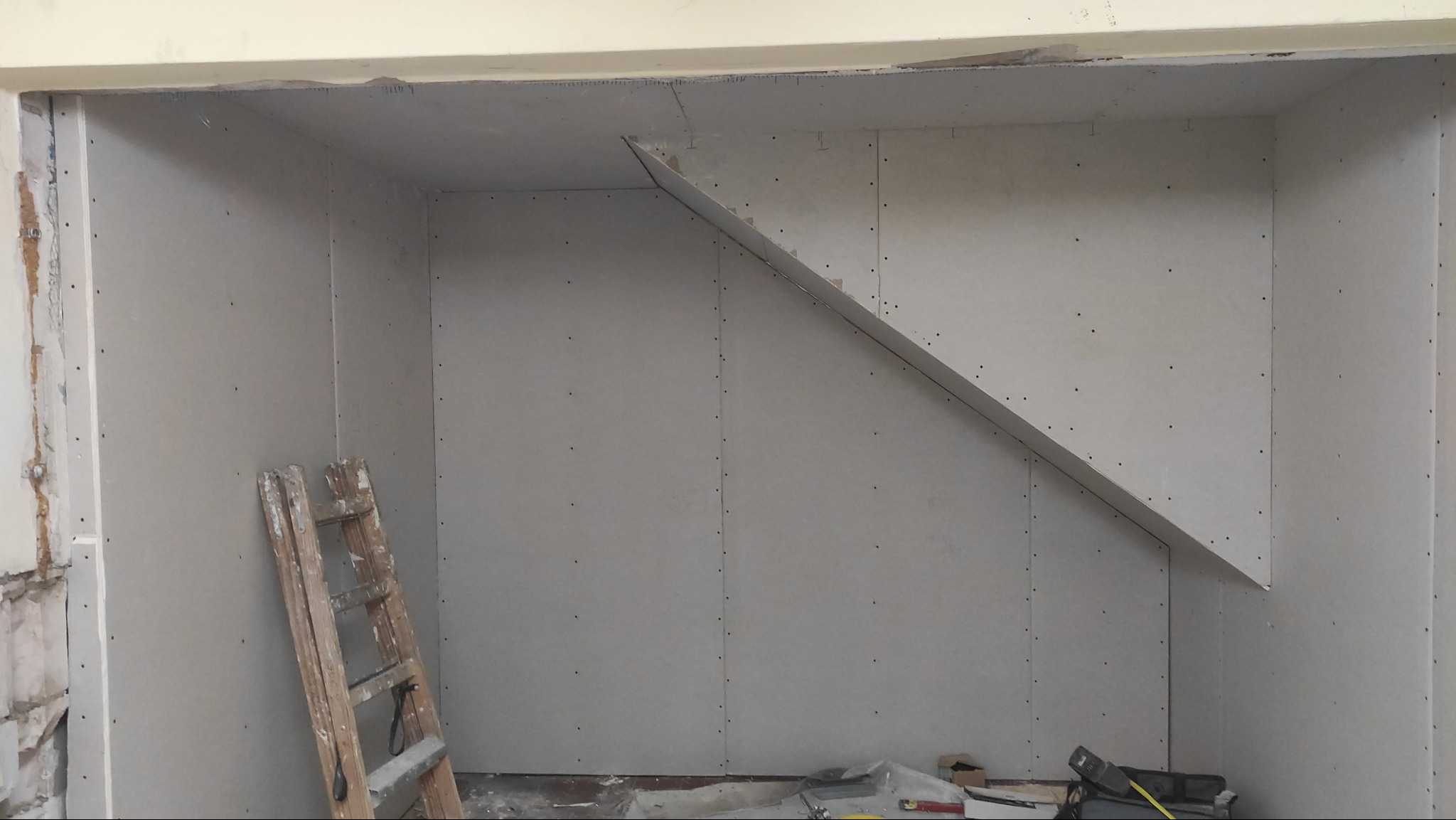 Płyty gipsowo-kartonowe na ścianach poddasza, widoczna drewniana drabina i narzędzia, przygotowanie do dalszych prac wykończeniowych.