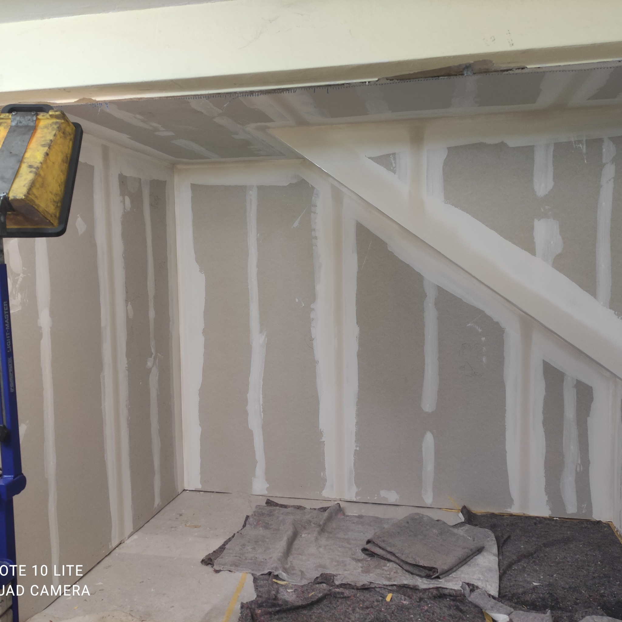 Wnętrze w trakcie szpachlowania: płyty gipsowo-kartonowe z widocznymi łączeniami, oświetlone lampą budowlaną, przygotowane do dalszych prac wykończeniowych.