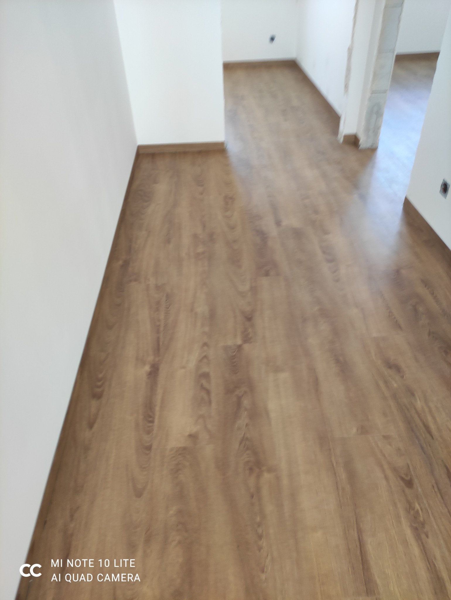 Ułożone panele podłogowe w korytarzu, widoczne białe ściany. Wykończenie w odcieniach brązu, perspektywa od dołu do góry. Widok na świeżo wykończone wnętrze.