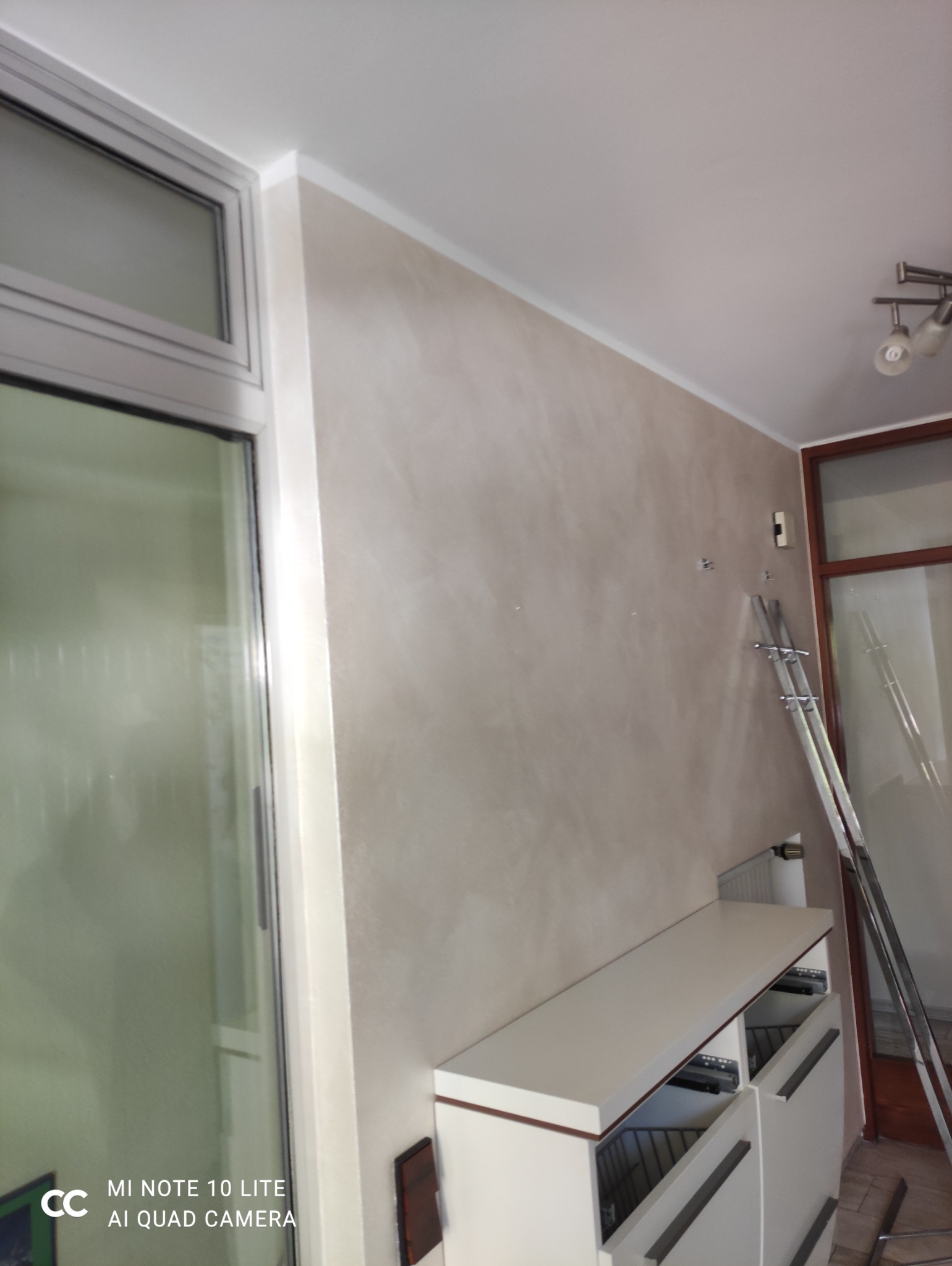 Ściana po dekoracyjnym malowaniu w odcieniach beżu, widoczna drabina, białe meble i okno. Efektowna faktura na ścianie.