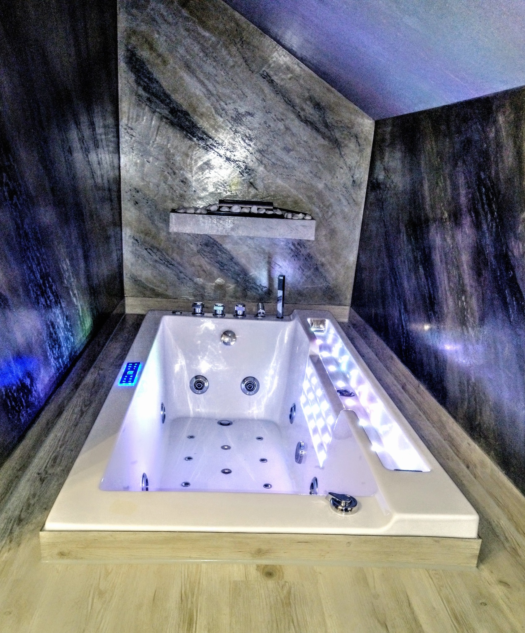 Nowoczesna wanna z hydromasażem, podświetlana LED, w łazience z dekoracyjną ścianą imitującą marmur. Wykończenie wnętrza w odcieniach szarości i bieli.