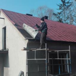 Normal-rembud Wojciech Rutkowski - Pracownik na rusztowaniu w Goleszowie demontuje starą blachę z dachu budynku jednorodzinnego z czerwonym pokryciem.