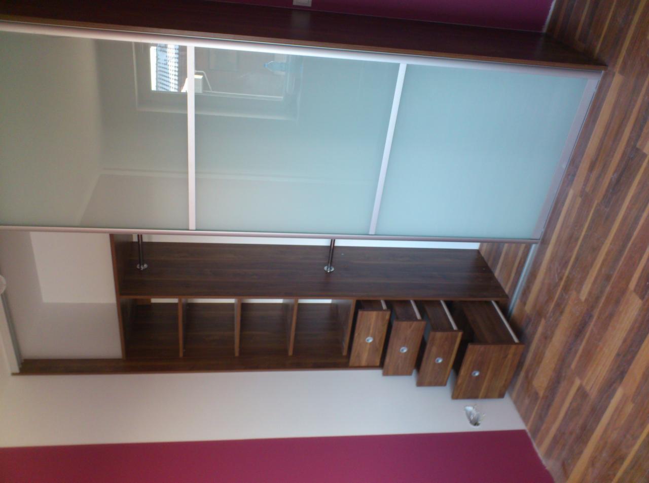 Wnętrze szafy wnękowej z przesuwnymi drzwiami z mlecznego szkła, widoczne półki i wysuwane szuflady z drewnianymi frontami i metalowymi uchwytami, wnętrze w odcieniach brązu i bieli, ściana...