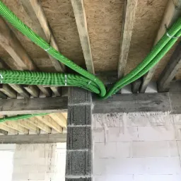 Zielone rury wentylacyjne przymocowane do drewnianej konstrukcji stropu w surowym wnętrzu budynku z białymi ścianami z betonu komórkowego i szarymi betonowymi słupami.