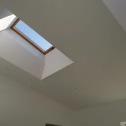 Białe wnętrze z oknem dachowym i wystającymi kablami elektrycznymi, widoczne fragmenty ścian i sufitu, świeżo po malowaniu.