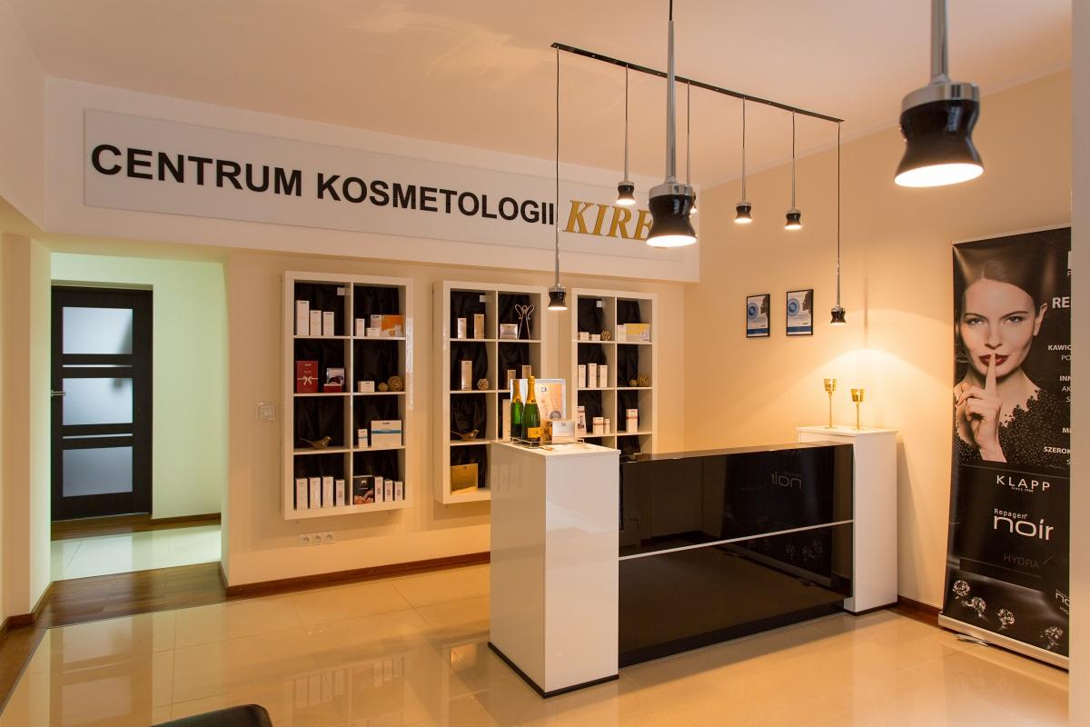 Nowoczesne wnętrze centrum kosmetologii z biało-czarną recepcją, oświetleniem punktowym i regałami z kosmetykami, uzupełnione plakatem reklamowym i butelkami szampana.